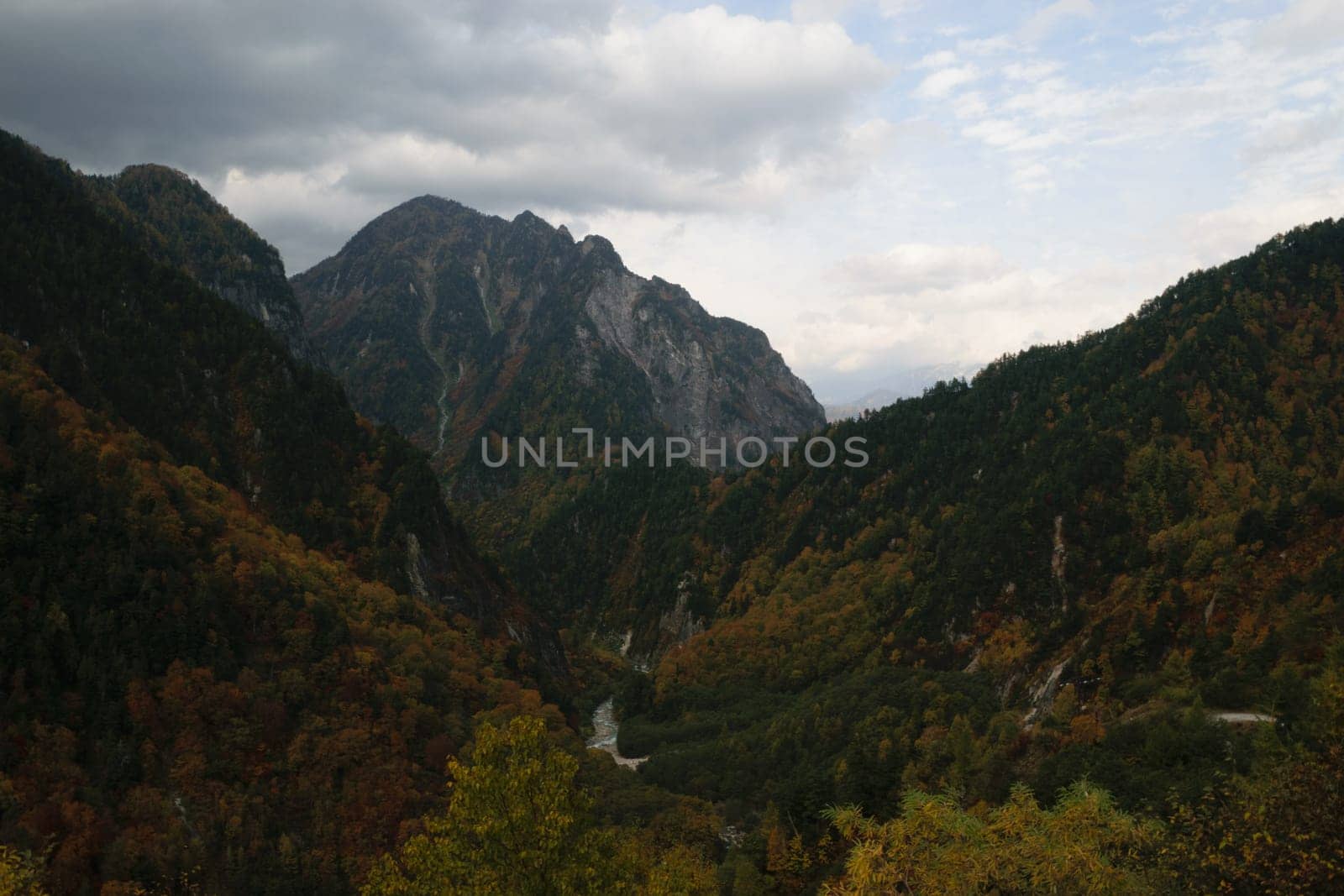 A scenic view of a mountainous landscape with a river flowing through a forested valley under a cloudy sky.