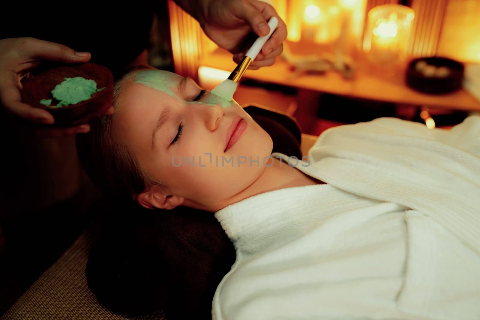 Serene ambiance of spa salon, woman customer indulges in rejuvenating with luxurious face cream massage with warm lighting candle. Facial skin treatment and beauty care concept. Quiescent