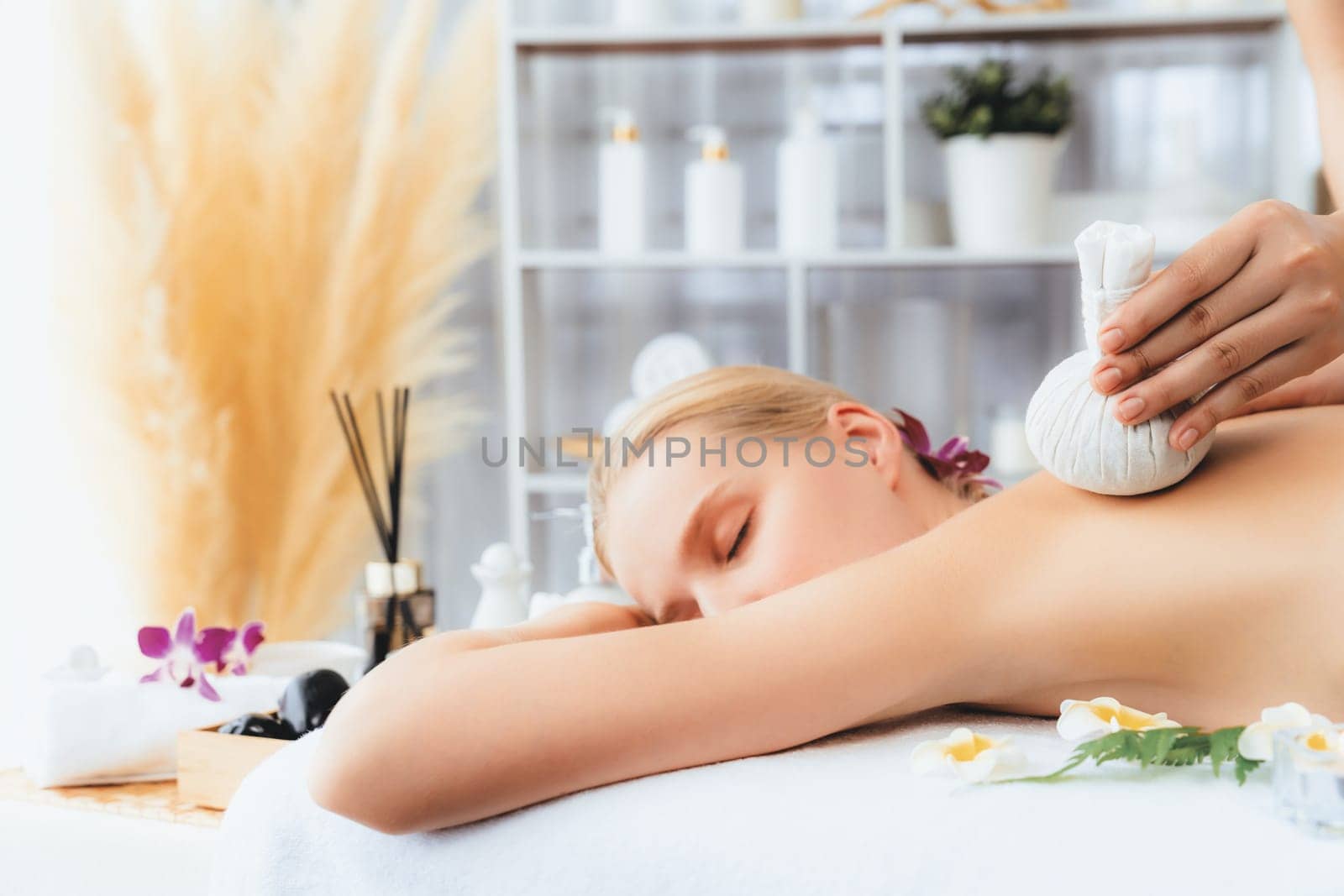 Hot herbal ball spa massage body treatment, masseur gently compresses herb bag on woman body. Tranquil and serenity of aromatherapy recreation in day lighting ambient at spa salon. Quiescent