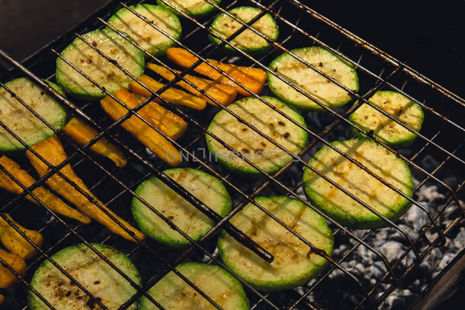 Chopped zucchini and carrots roasting on fire seasoned with aroma herbs and spices. Delicious fresh vegetables grilling on barbecue smoker grid. Diet vegan bbq. Outdoor recreation in backyard