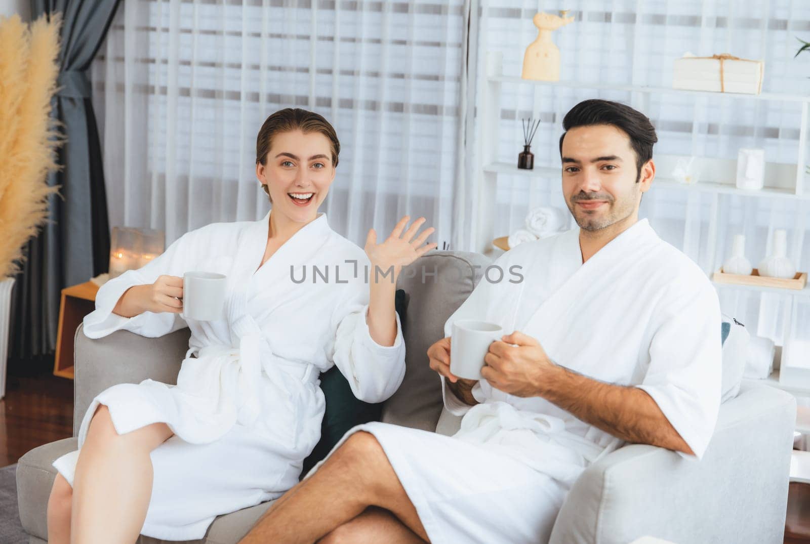 Beauty or body treatment spa salon vacation lifestyle concept with couple wearing bathrobe relaxing with drinks in luxurious hotel spa or resort room. Vacation and leisure relaxation. Quiescent