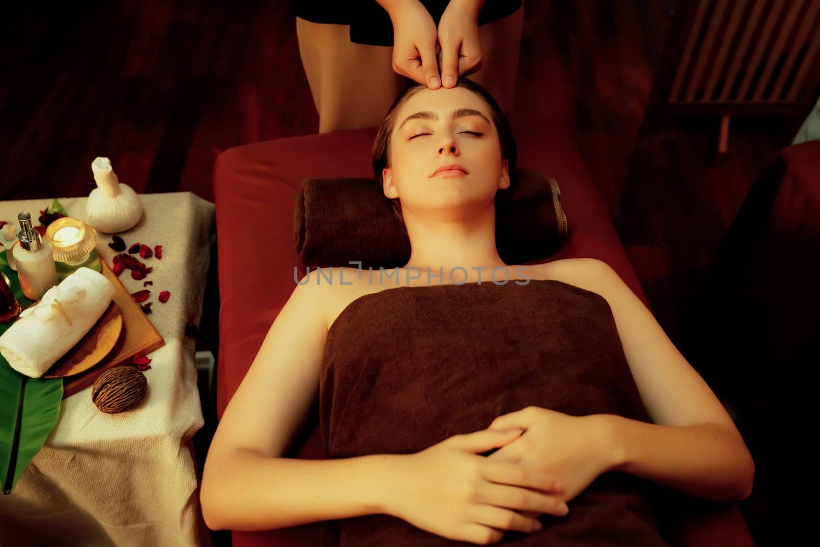 Caucasian woman enjoying relaxing anti-stress head massage and pampering facial beauty skin recreation leisure in warm candle lighting ambient salon spa in luxury resort or hotel. Quiescent