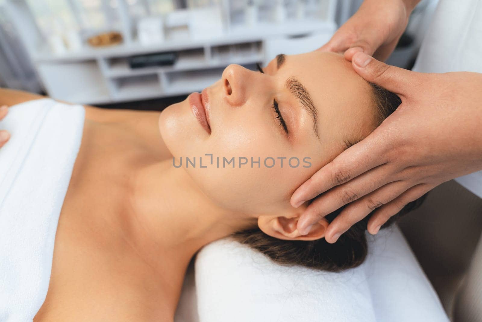 Caucasian woman enjoying relaxing anti-stress head massage and pampering facial beauty skin recreation leisure in dayspa modern light ambient at luxury resort or hotel spa salon. Quiescent