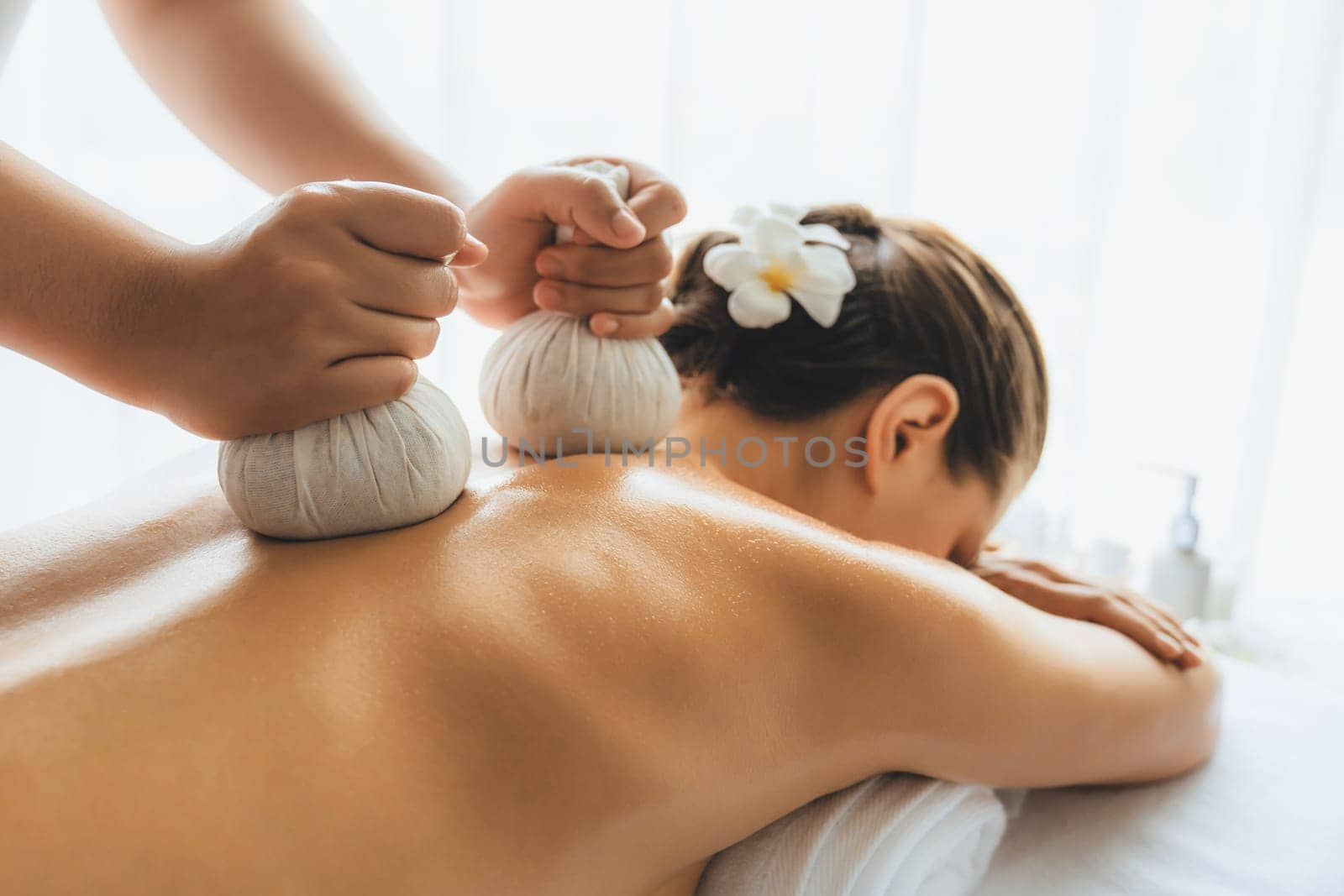 Hot herbal ball spa massage body treatment, masseur gently compresses herb bag on woman body. Tranquil and serenity of aromatherapy recreation in day lighting ambient at spa salon. Quiescent