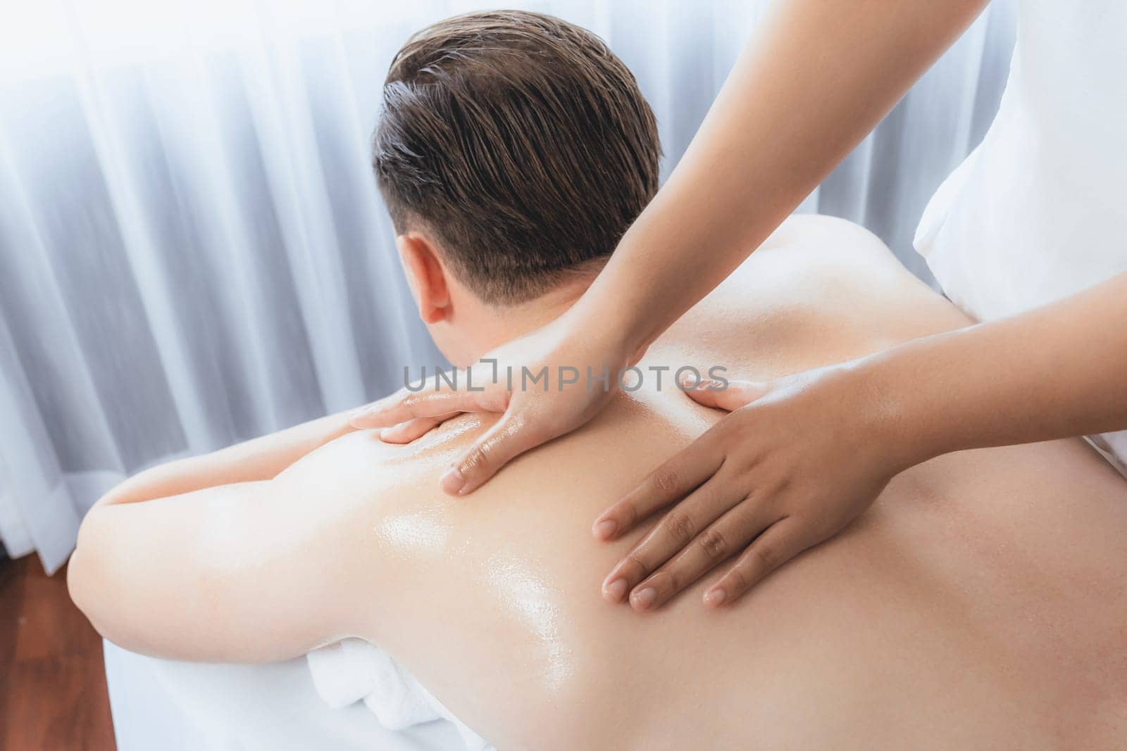 Caucasian man customer enjoying relaxing anti-stress spa massage and pampering with beauty skin recreation leisure in day light ambient salon spa at luxury resort or hotel. Quiescent