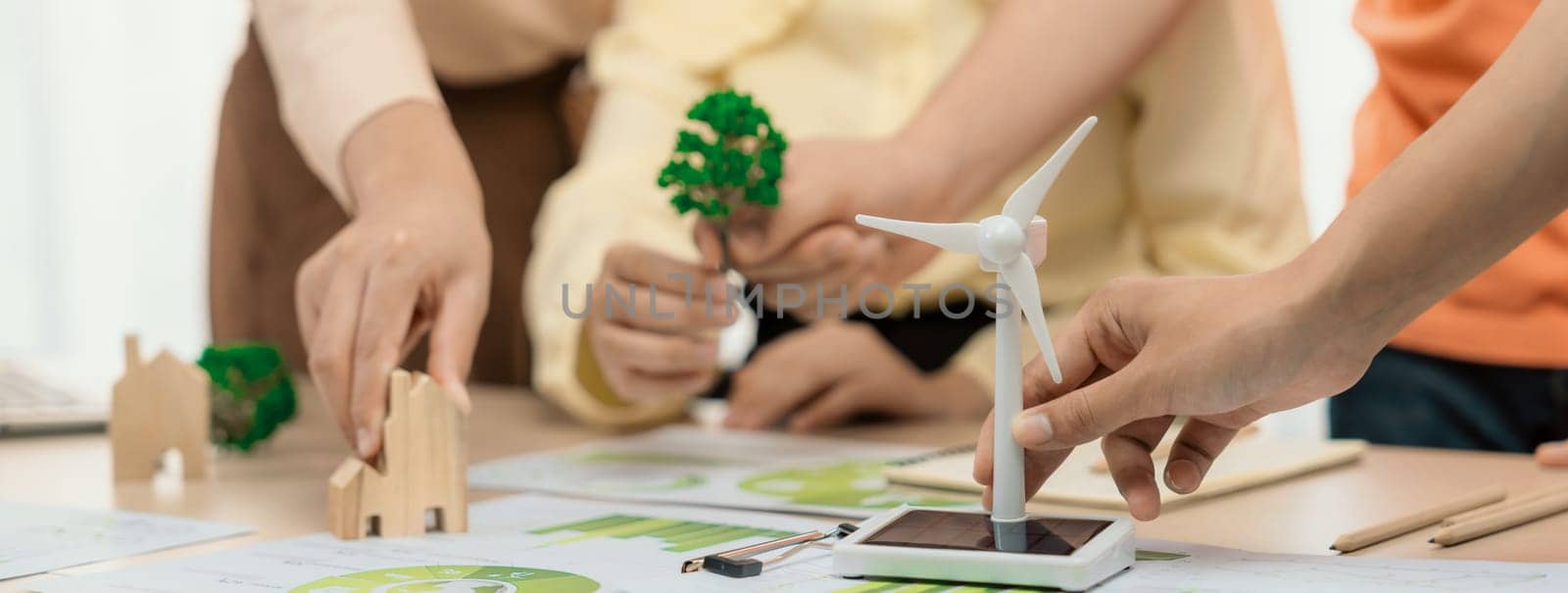 Windmill model represented using renewable energy placed during presenting green business on table with wooden block and environmental document scatter around. Closeup. Delineation.