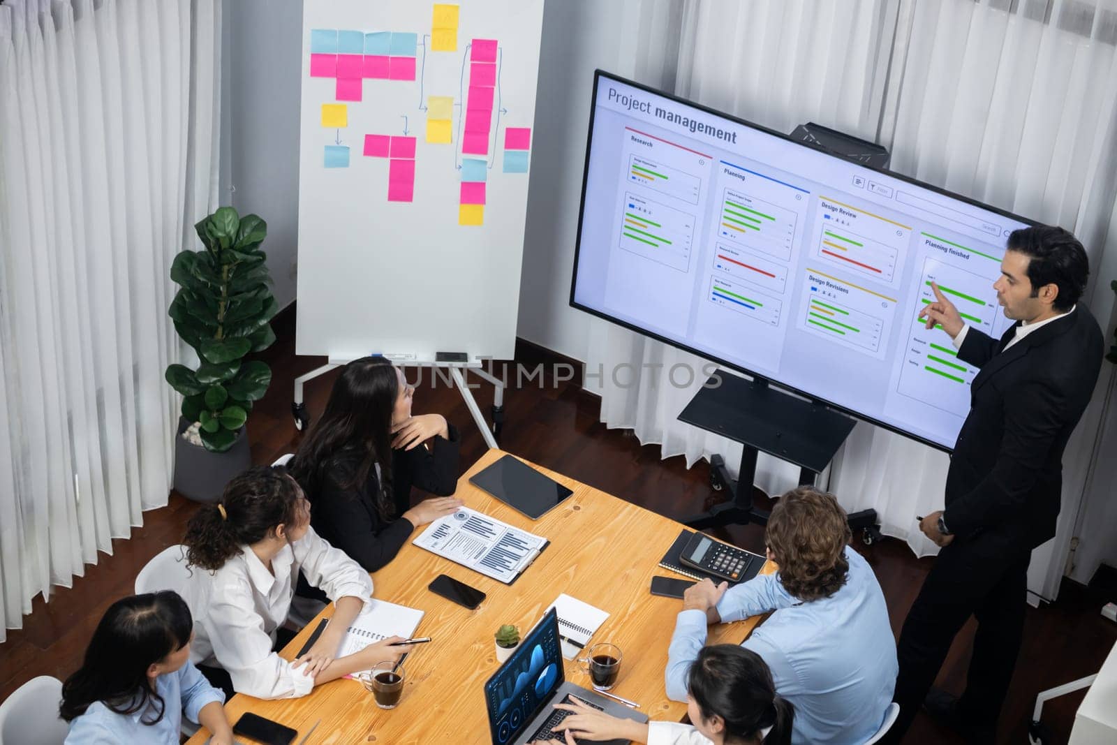 Project manager planning schedules for business task at meeting room, Gantt chart software show on TV screen. Multi ethnic diversity business people and modern business project management. Meticulous