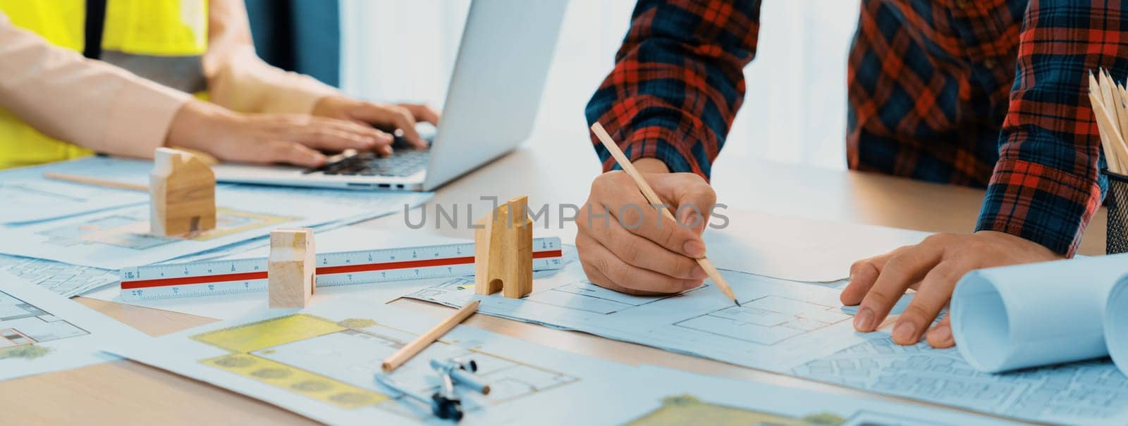 A cropped portrait of professional architect working with blueprint during safety engineer using laptop analysis data at meeting table with document scatter around. Close up. Delineation.
