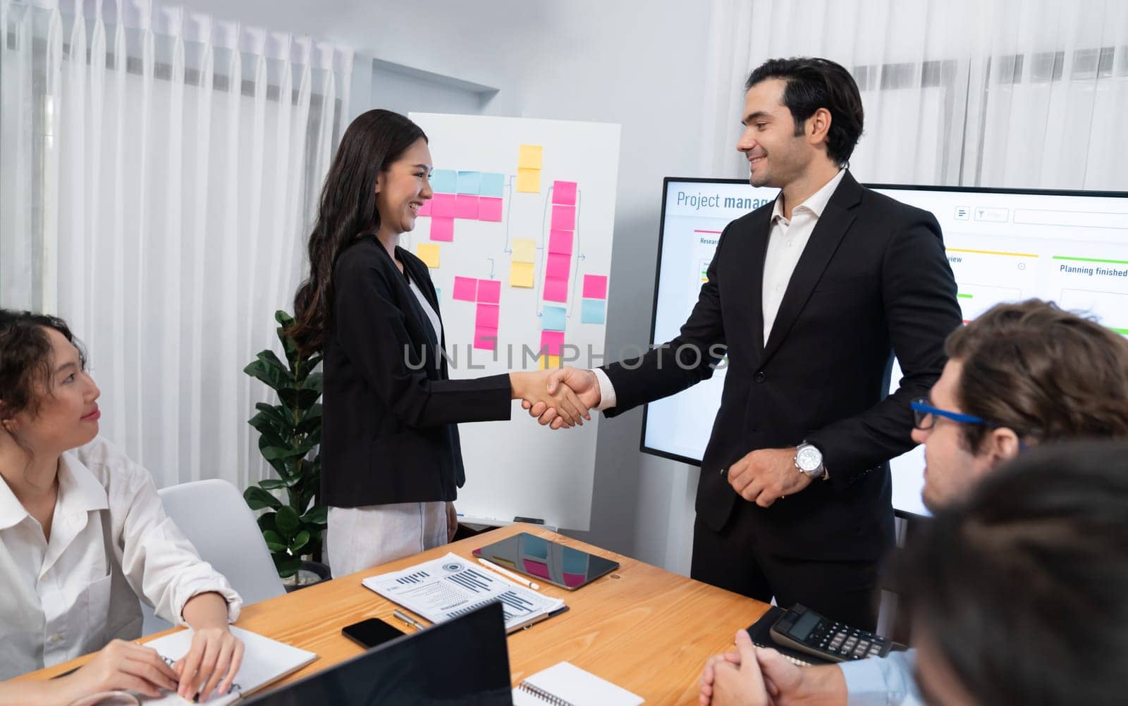 Cheerful meeting room, businesspeople celebrate with handshaking. Successful project was completed before the deadline. Business partnership and collaboration in project management. Habiliment