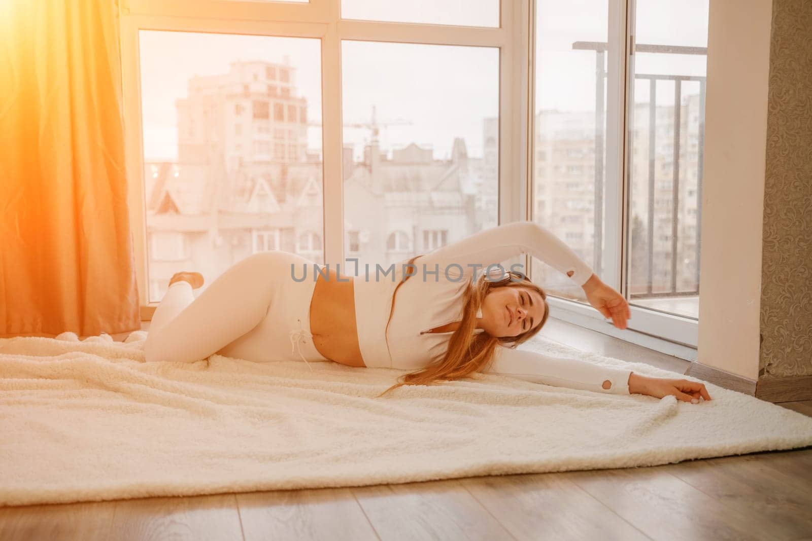 Side view portrait of relaxed woman listening to music with headphones lying on carpet at home. She is dressed in a white tracksuit