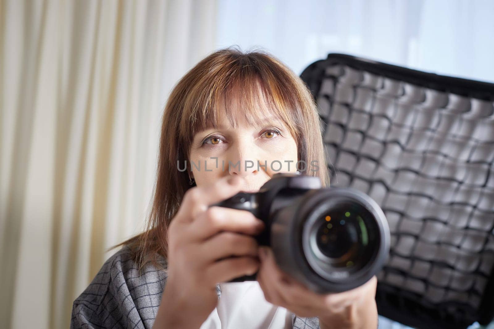 Senior old elderly woman with black camera with a large lens indoors in the studio. Professional photographer. Age Hobby