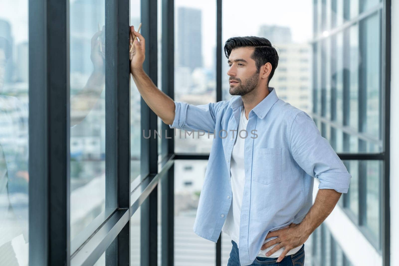 Skilled businessman standing at office surrounded by skyscraper view. Smart architect engineer wear casual outfit standing near panoramic window while looking at city view. Success business. Tracery.
