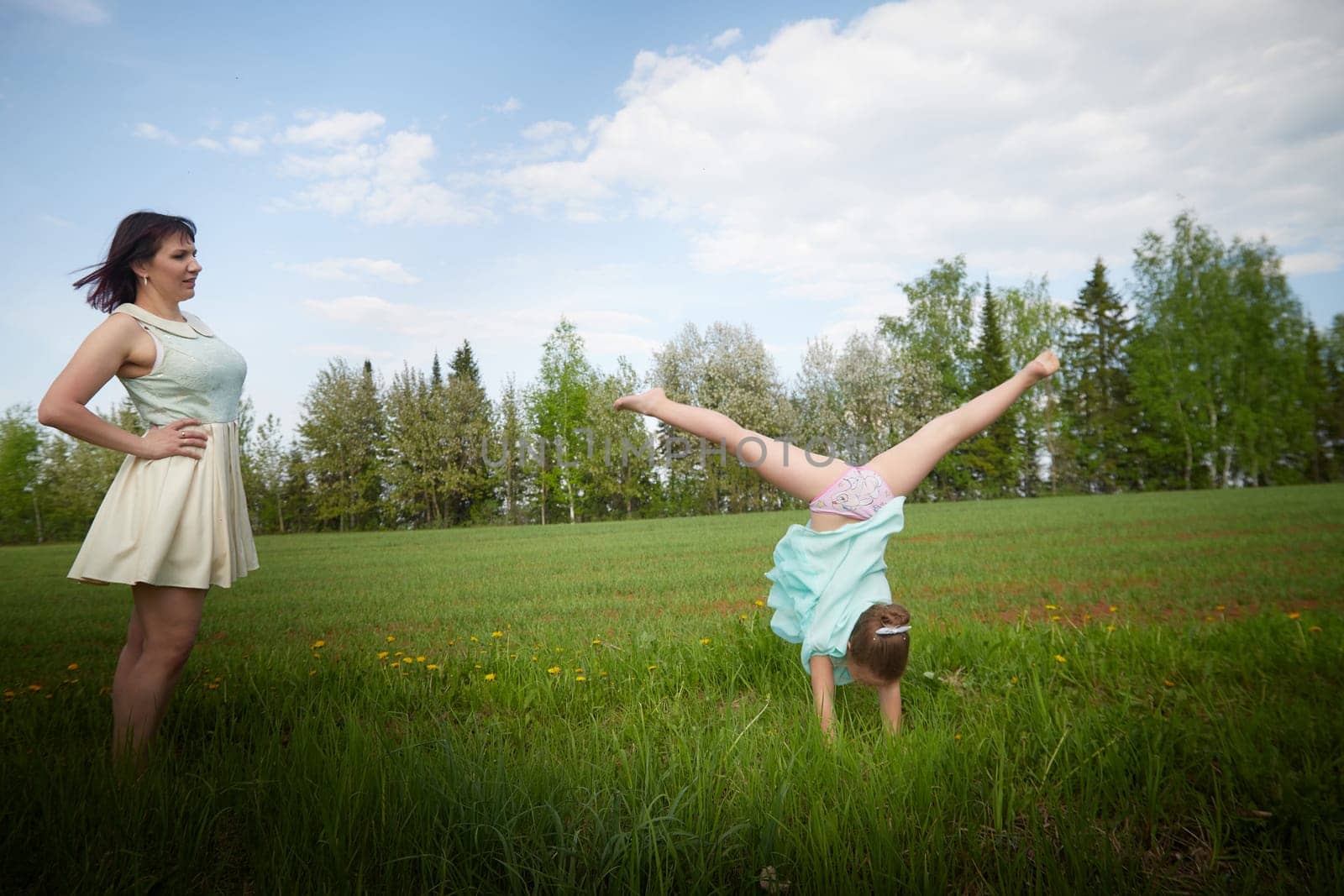 Happy mother and daughter enjoying rest, playing, fun and doing sports exercises on nature in a green field. Woman and girl resting outdoors in summer and spring day