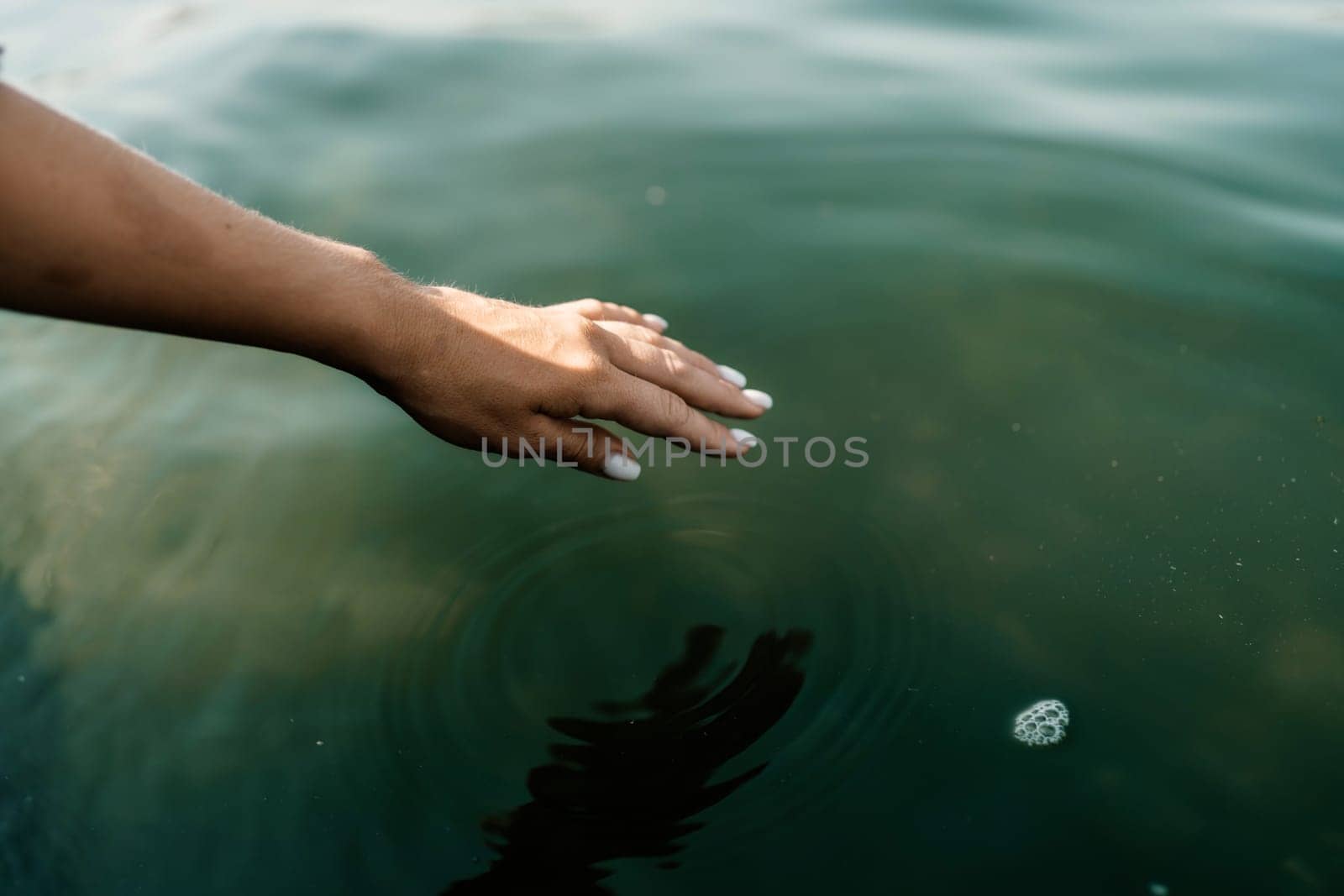 The hand touches the water, creating ripples. The water is calm and clear, and the hand is white. Concept of tranquility and peacefulness