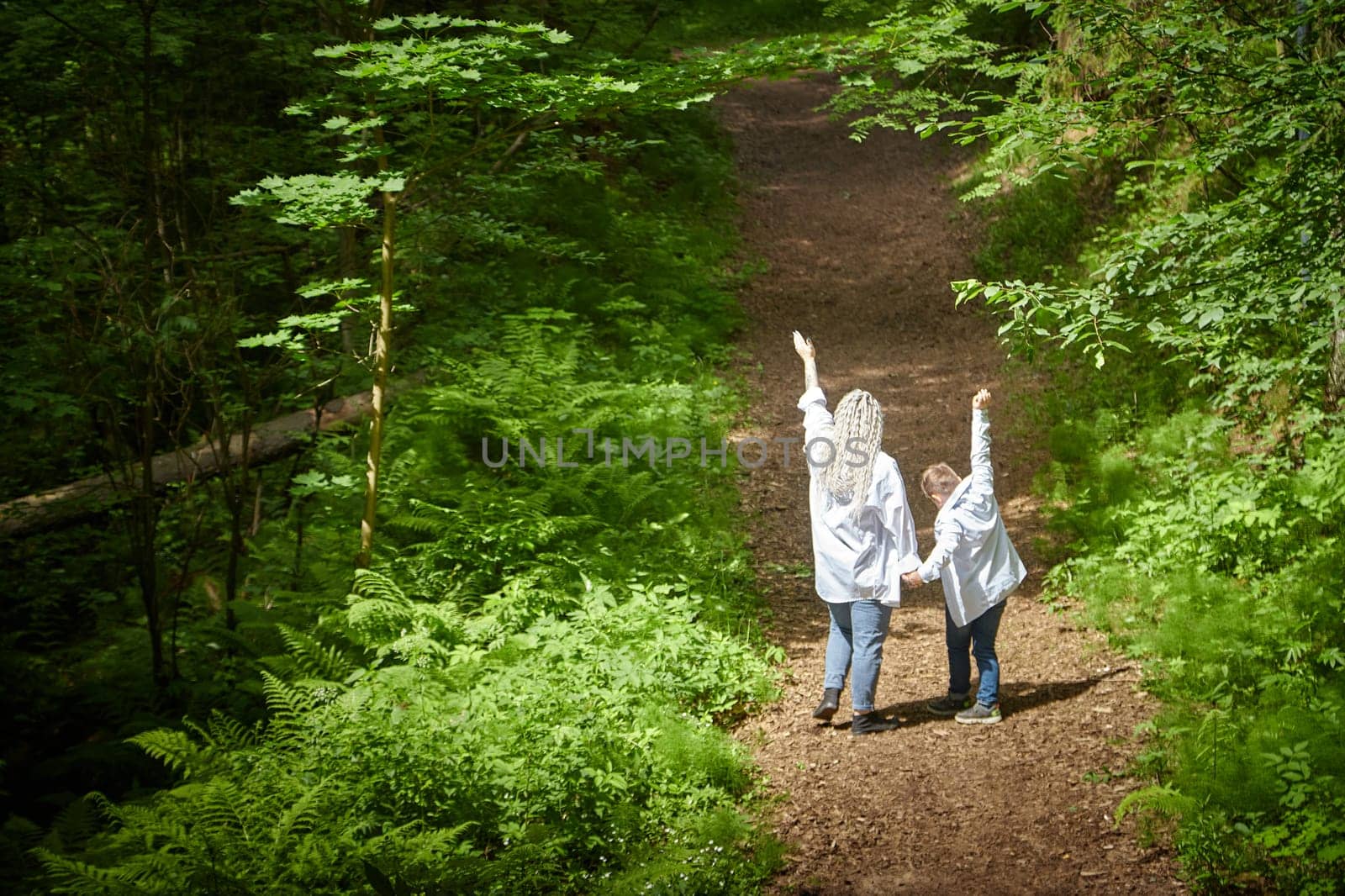 Funny mother with dreadlocks and fat boy happy walking in the forest on a sunny summer day