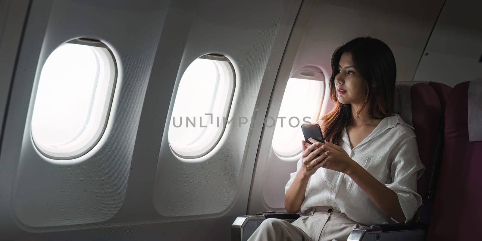 Asian business woman on aeroplane using smartphone.