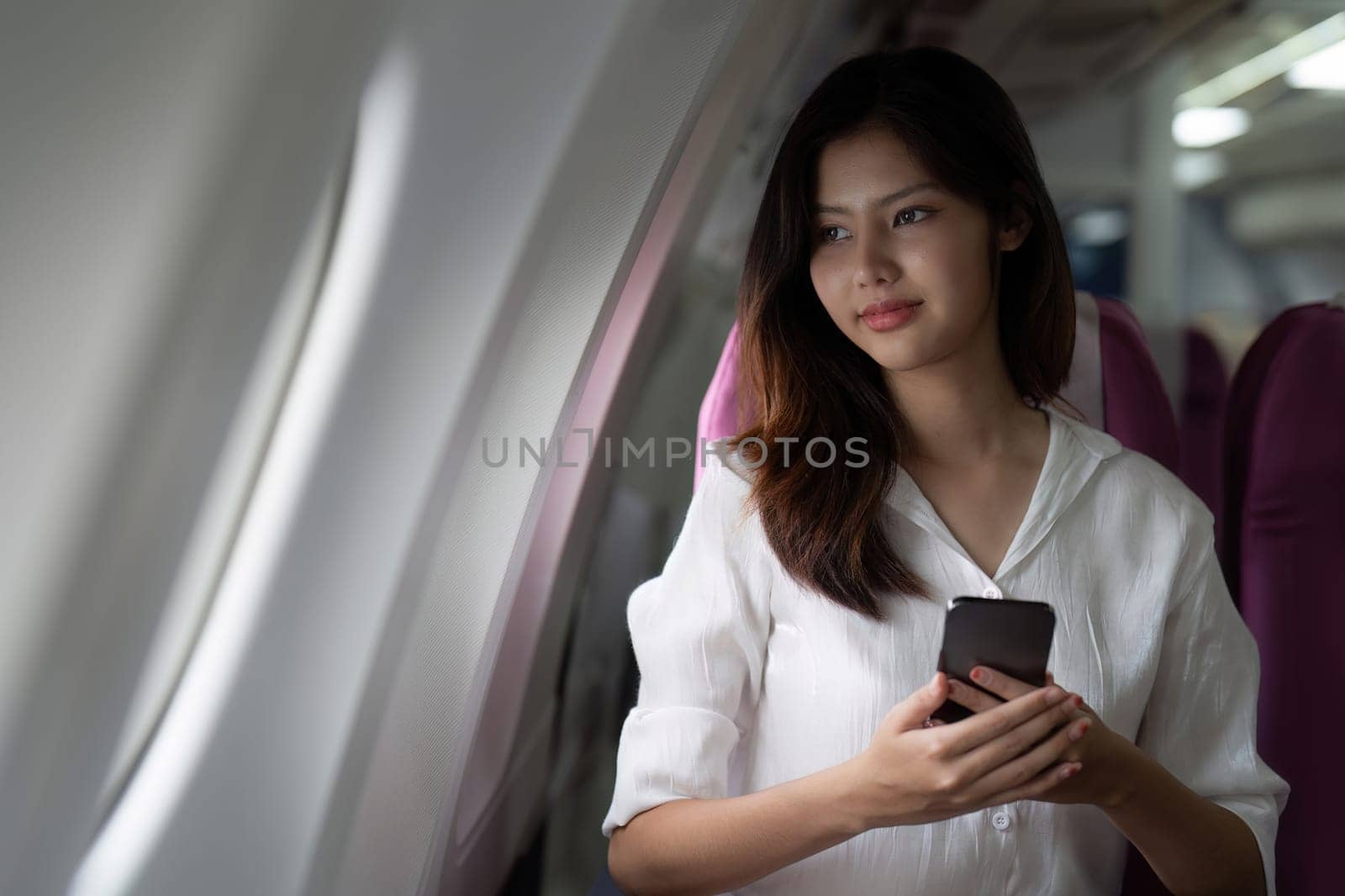 Asian business woman on aeroplane using smartphone.