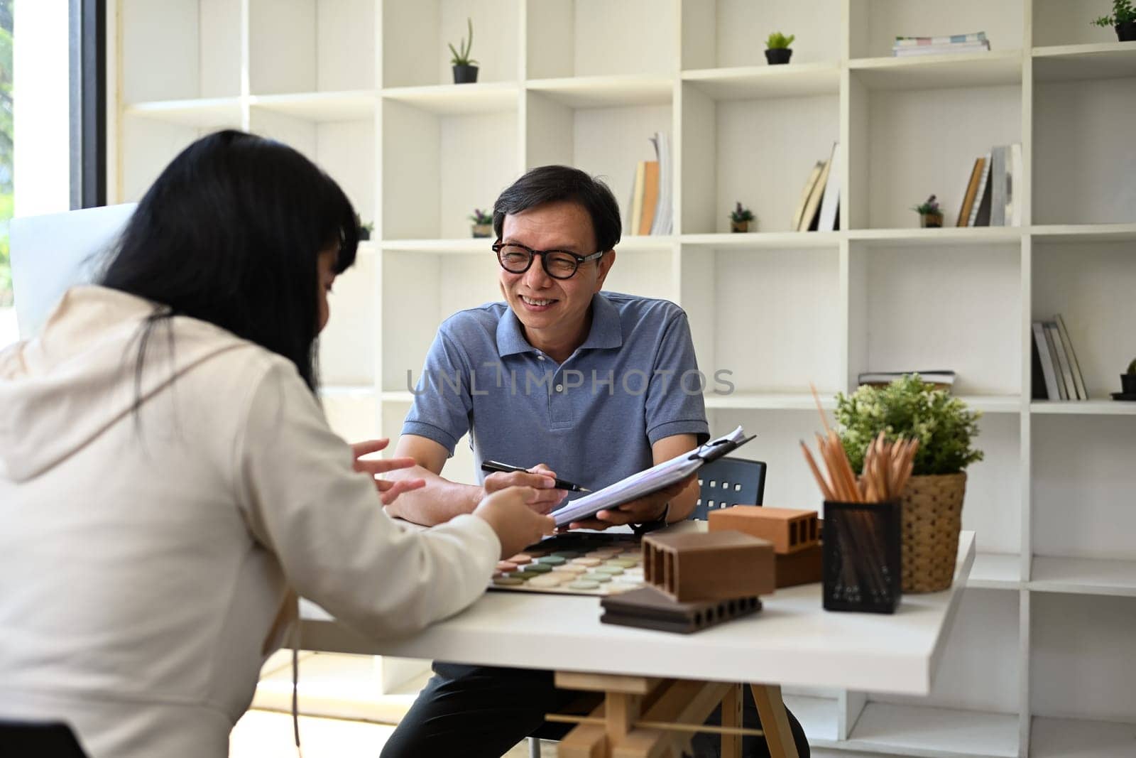 Senior male interior designer discussing building plan design project with his client at office.