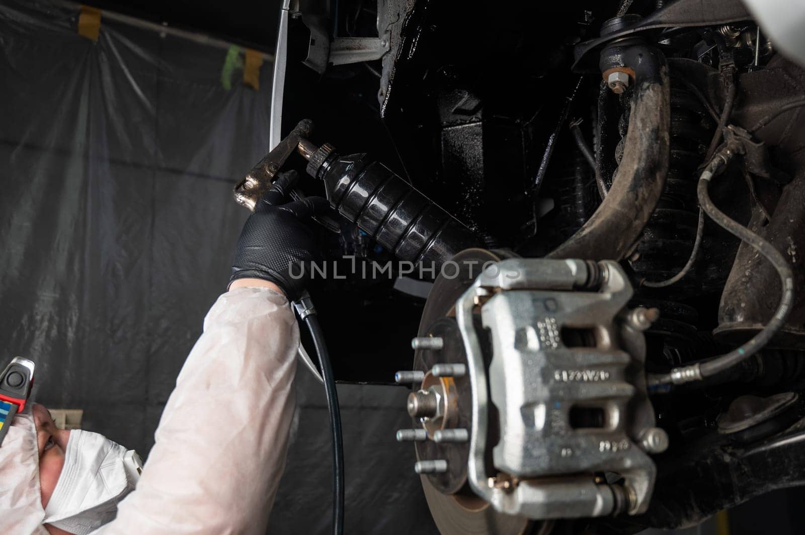 An auto mechanic applies anti-corrosion mastic to the underbody of a car