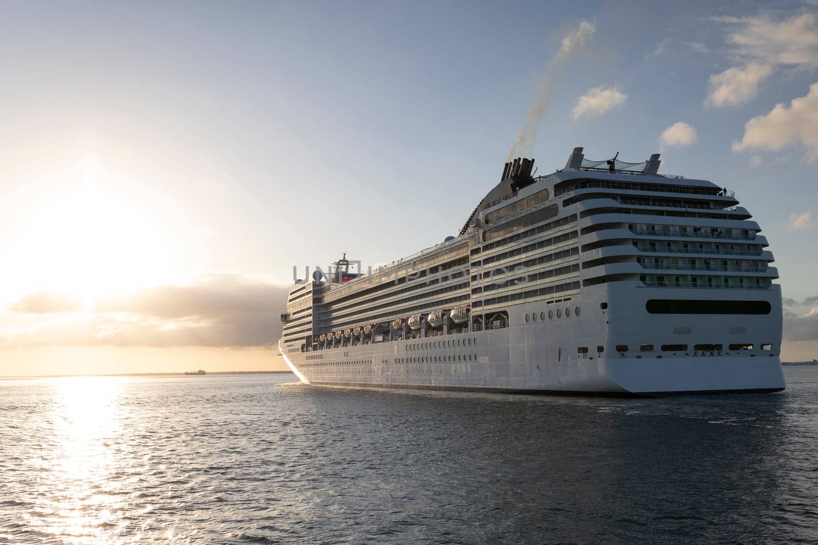 A large cruise ship with the letters MSC on the side is sailing in the ocean. The sun is setting in the background, creating a beautiful and serene atmosphere