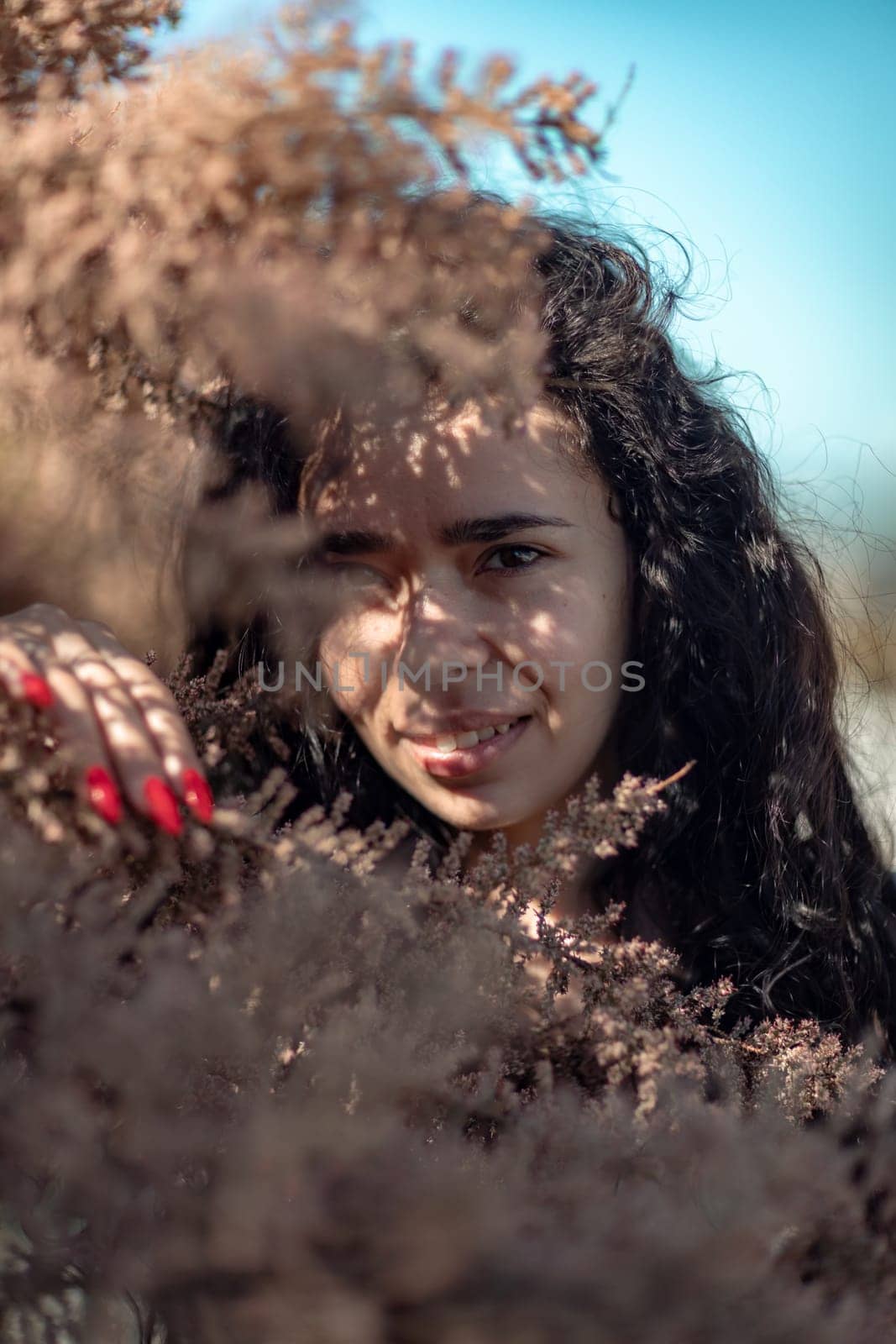 A woman is standing in a field of brown leaves. She is looking at the camera with a serious expression