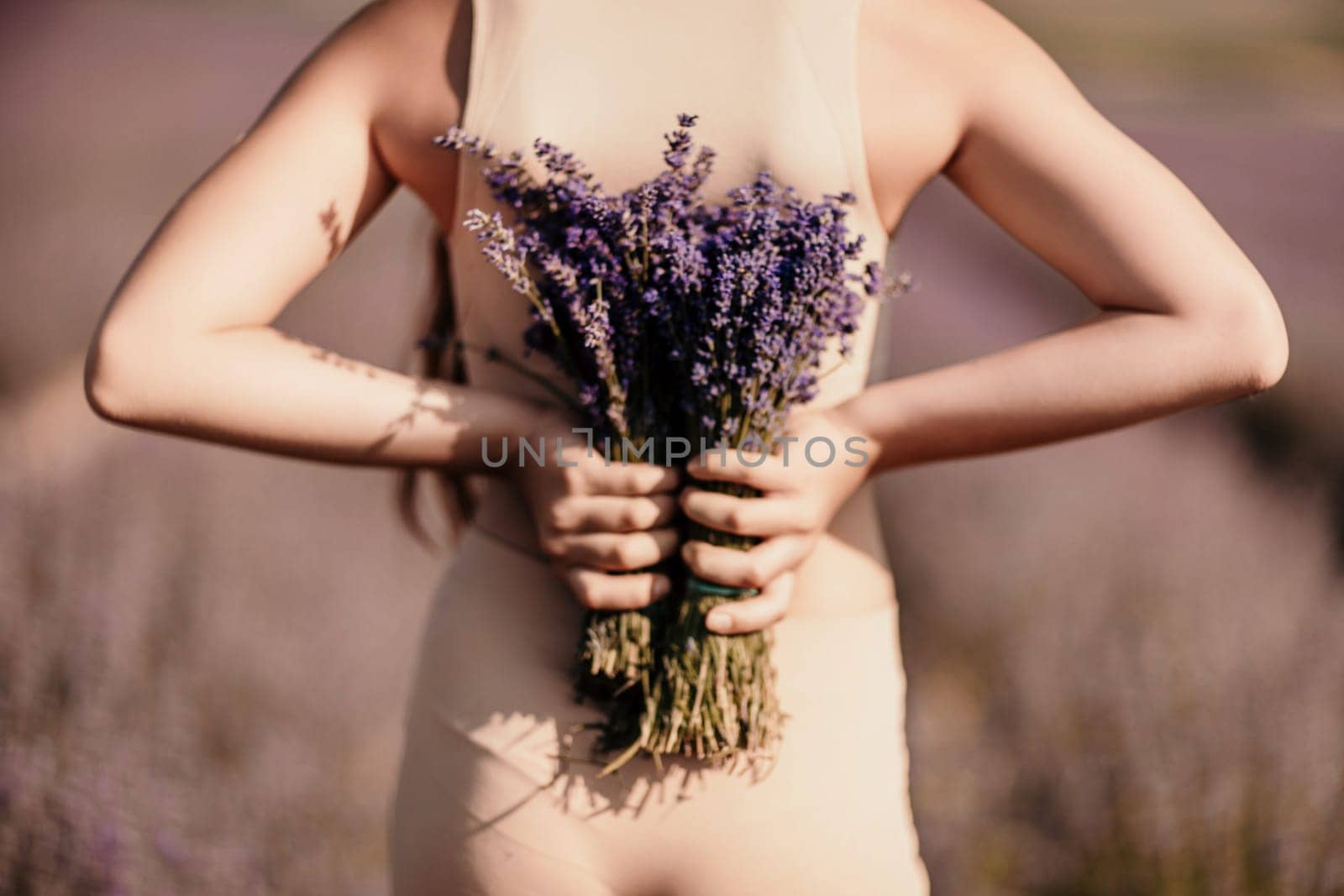 girl holding bouquet lavender flowers. The flowers are purple and the woman is wearing a tan top. Concept of calm and relaxation, as lavender is often associated with these feelings