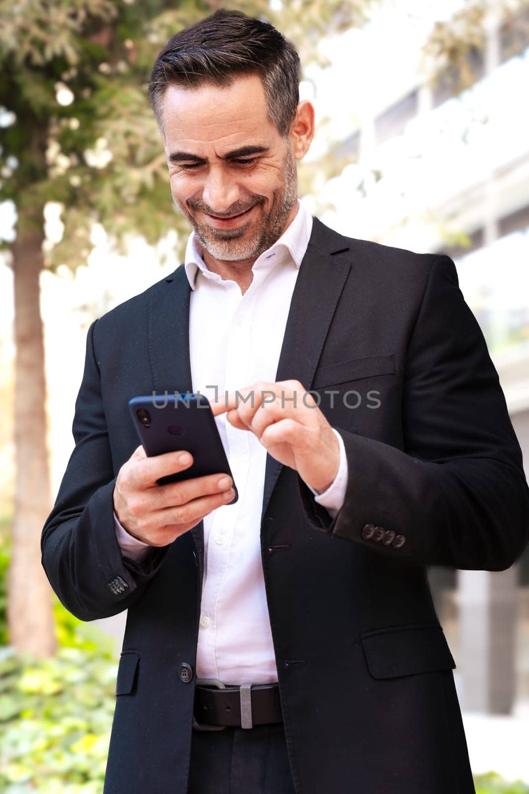 Vertical portrait businessman using an app on his smartphone and standing outdoors by mariaphoto3