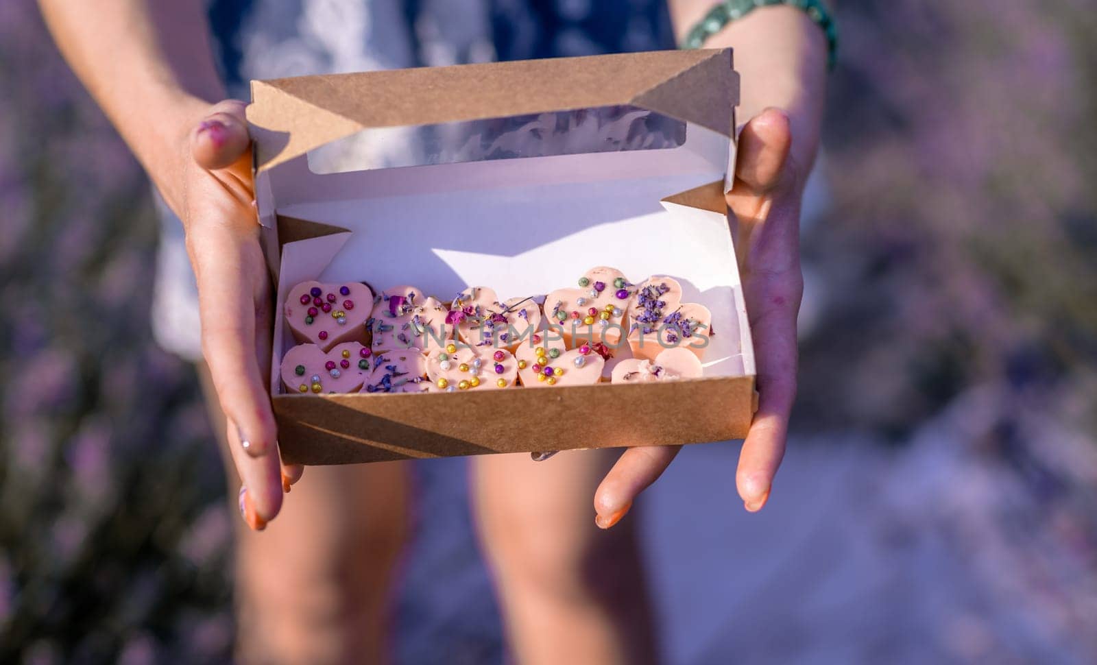 A person is holding a box of chocolate truffles. The box is white and brown, and the truffles are covered in colorful sprinkles