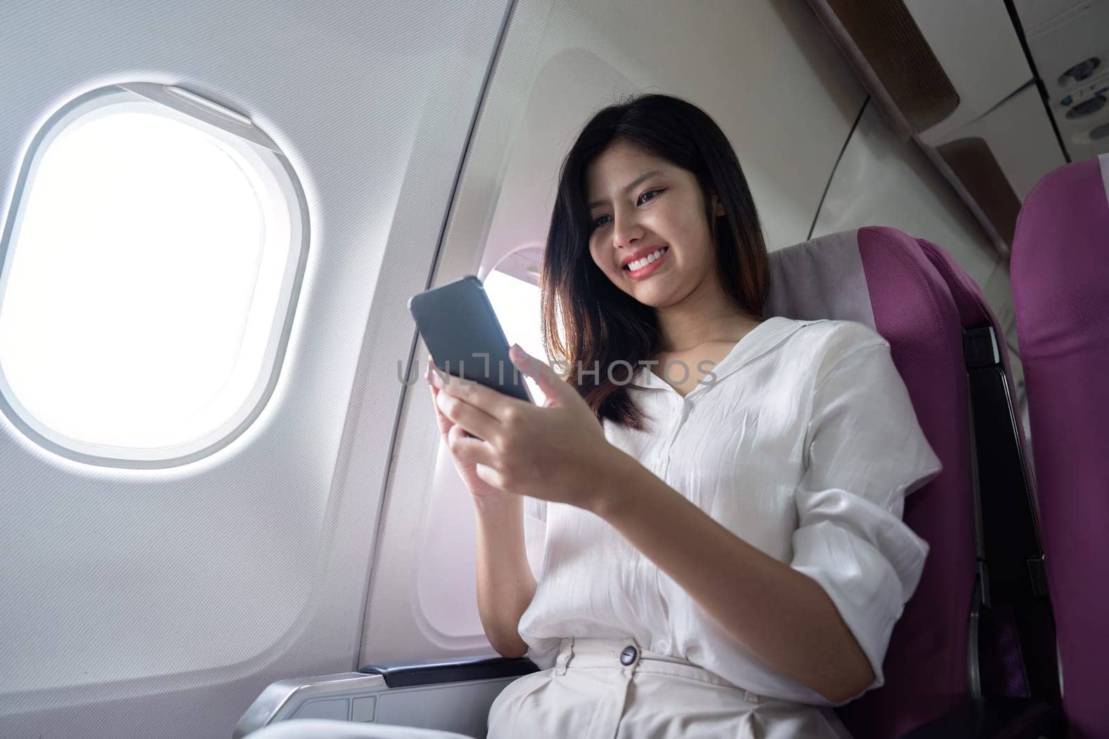Businesswoman using smartphone in airplane seat. Concept of business travel and digital connectivity.