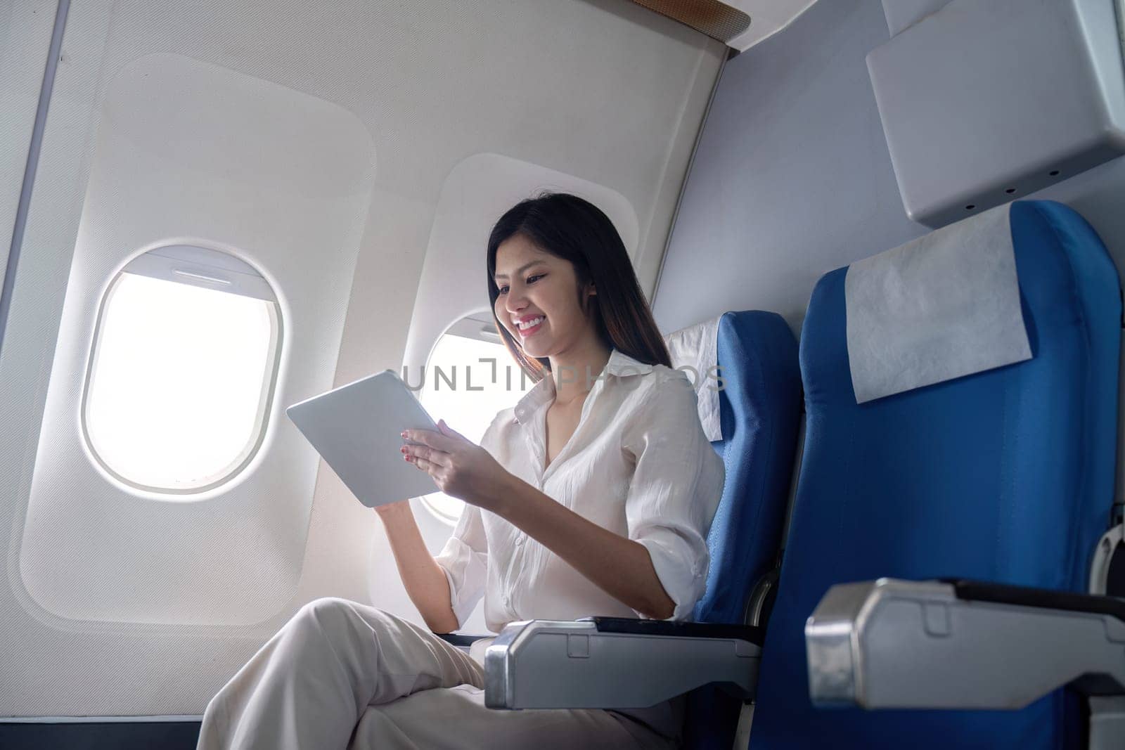 Businesswoman using tablet on airplane. Concept of business travel and digital connectivity.