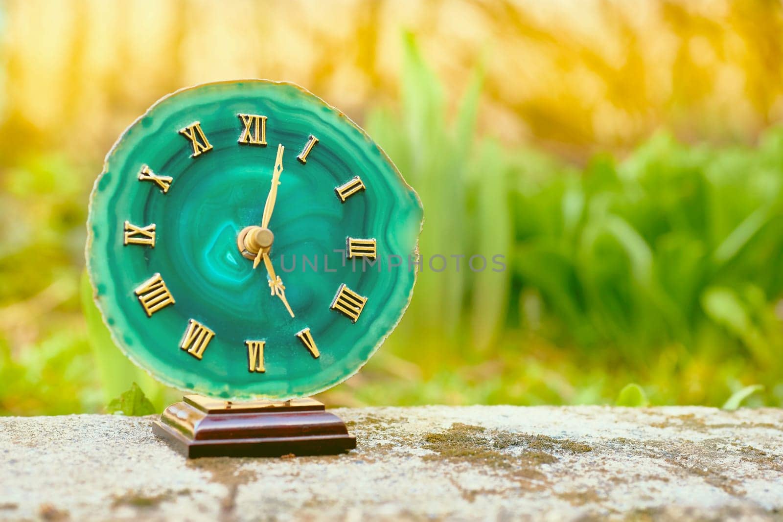 Clock with emerald dial. Gold numbers and arrows. Old stone among greenery by jovani68