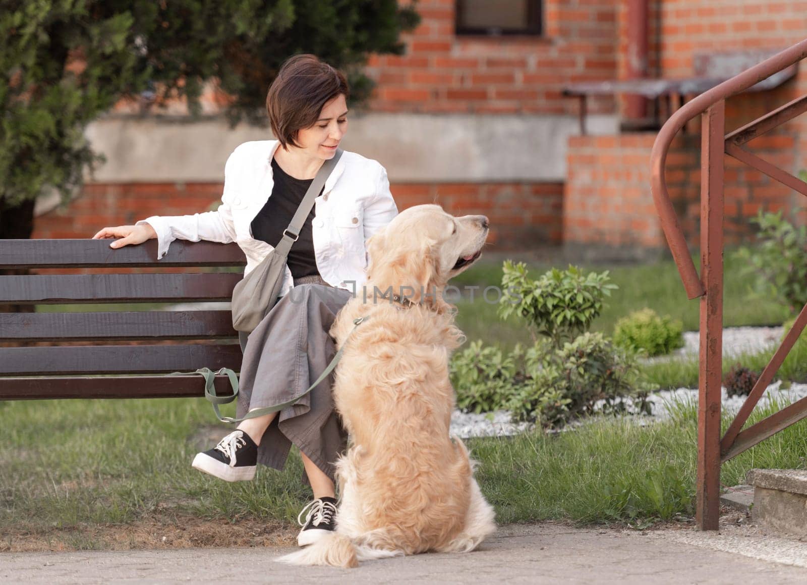 Young Woman Sits On Bench Near House With Golden Retriever by tan4ikk1