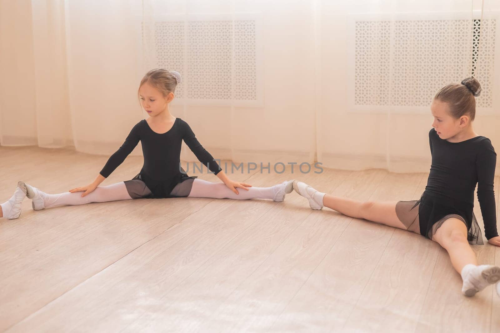 Little girls sit in a circle and do stretching at a ballet school