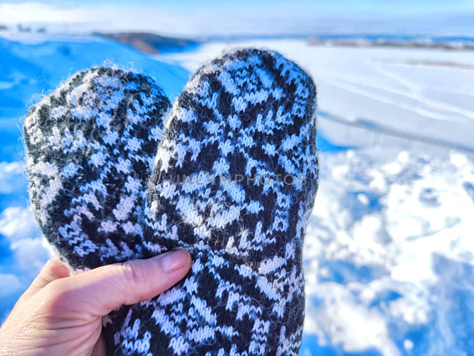 A hand with patterned woolen mittens gives thumbs up against a clear, snowy landscape