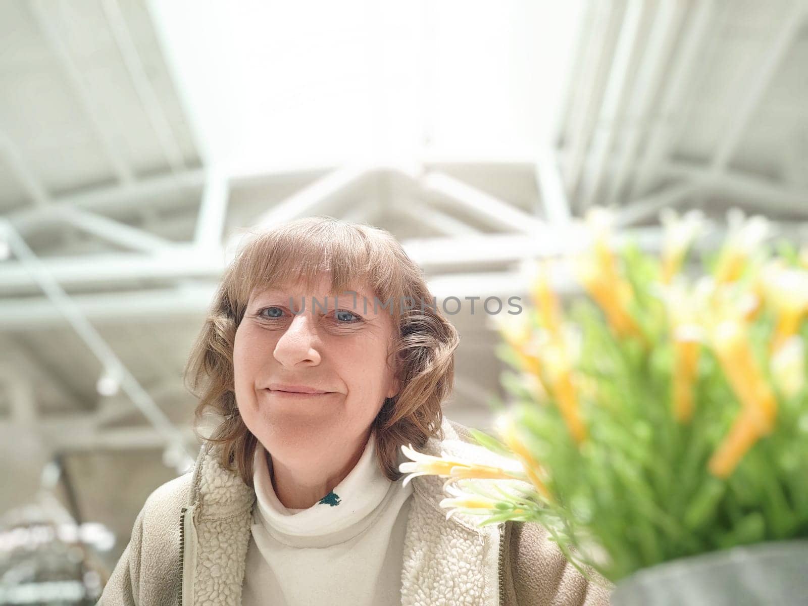 A woman smiles while taking a selfie in a brightly lit store filled with various products, including outdoor furniture.