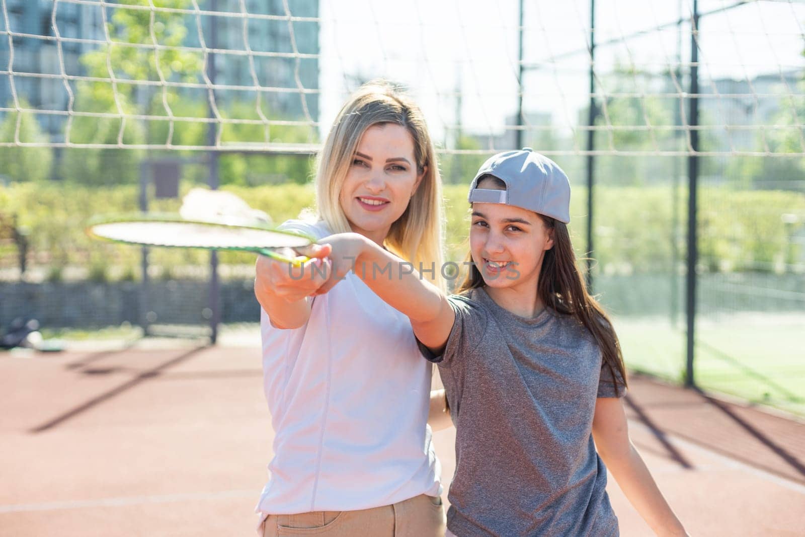 Mother and daughter are playing badminton outside in the yard on summer hot day . High quality photo