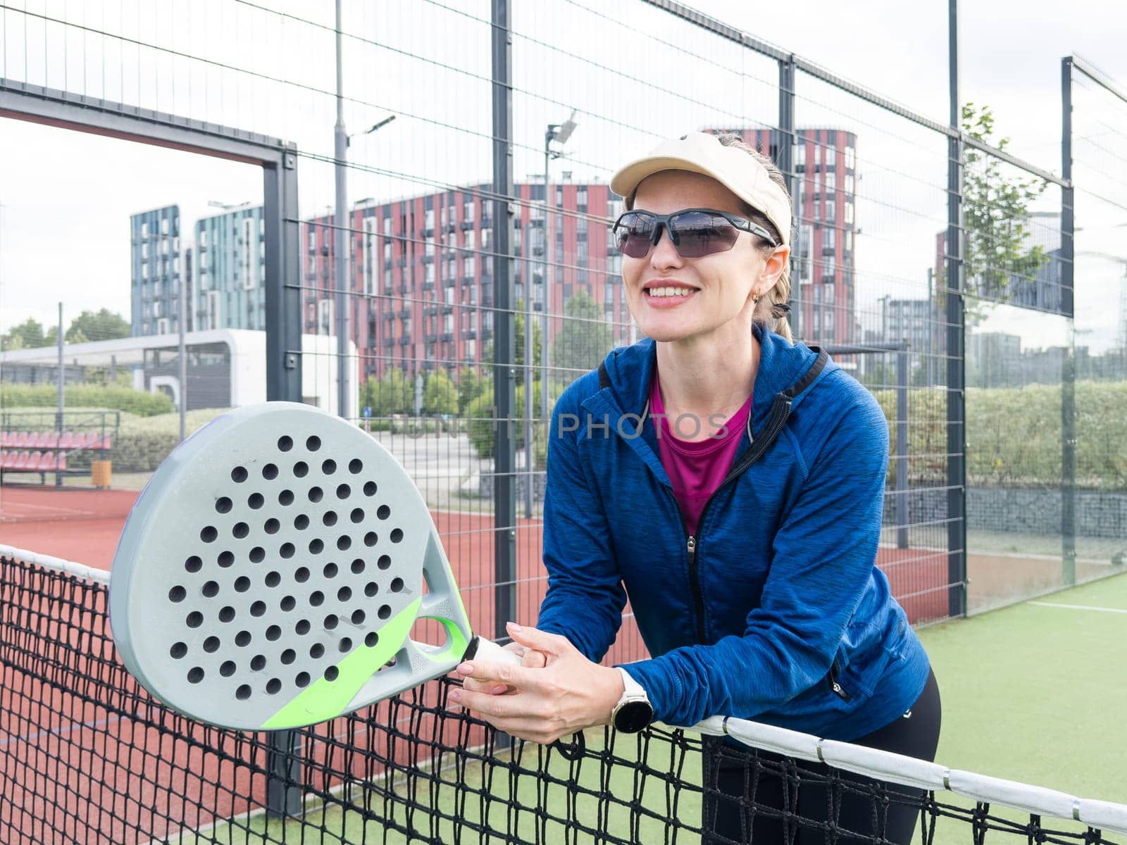 Portrait of positive young woman with racket and padel ball on tennis court. High quality photo