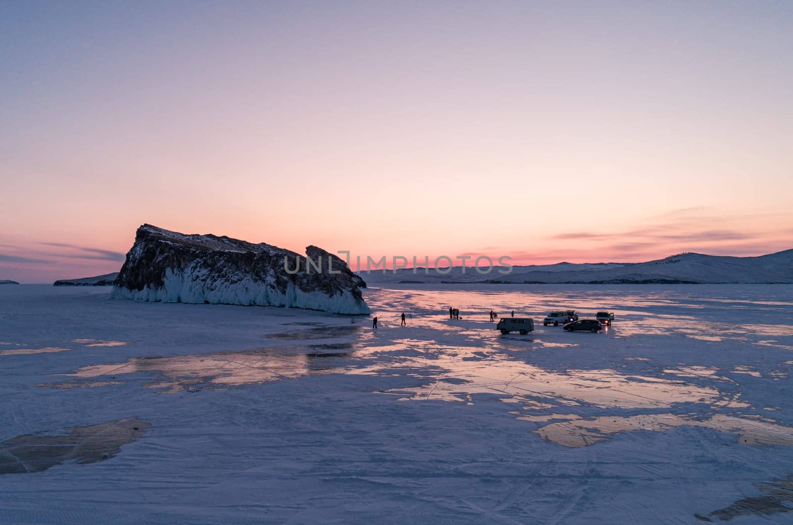 Aerial winter landscape of frozen lake Baikal. Groups of tourists got off the cars and walking around the rocky island in lake Baikal, walking on the crystal clear ice at sunrise. Famous tourist spot