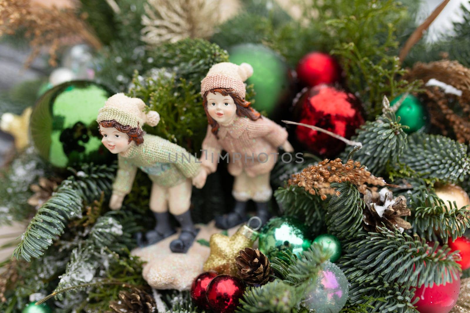 Two figurines, one of a snowman and the other of Santa Claus, are placed perched on the very top of a decorated Christmas tree. The snowman holds a tiny broom while Santa holds his bag of gifts, both appearing to be in a jolly and festive mood.