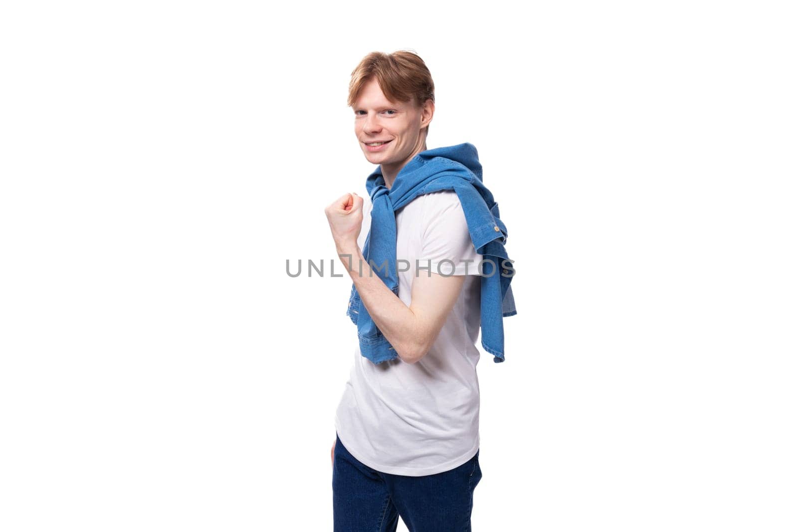 young well-groomed cute caucasian male student with golden red hair with a tattoo on his arms is dressed in a white t-shirt.