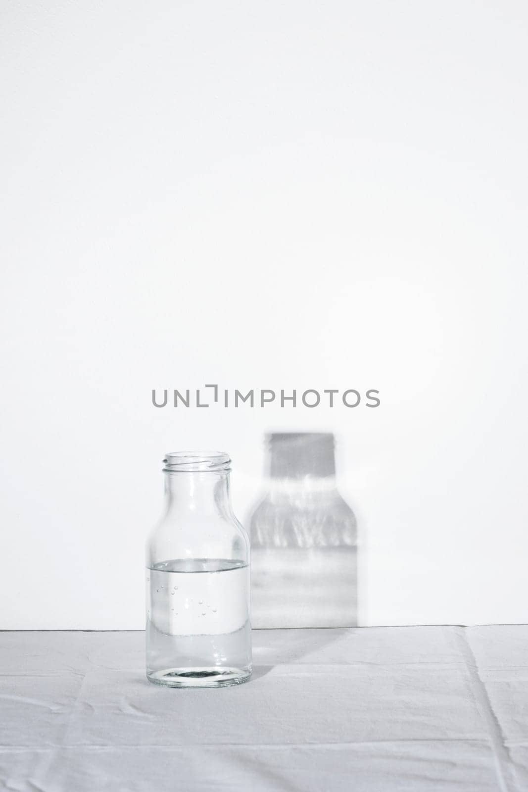 Empty transparent Glass Water bottle with shadow on white table and background with hard light, concept of pure still water