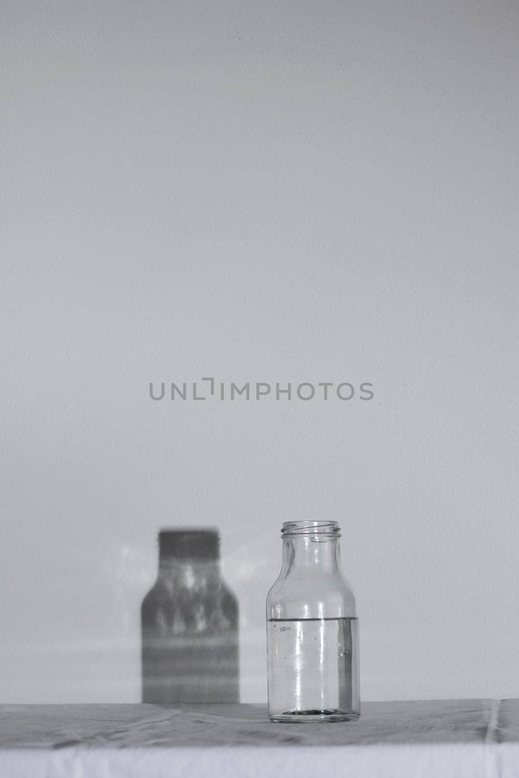 Empty transparent Glass Water bottle with shadow on white table and background with hard light, concept of pure still water