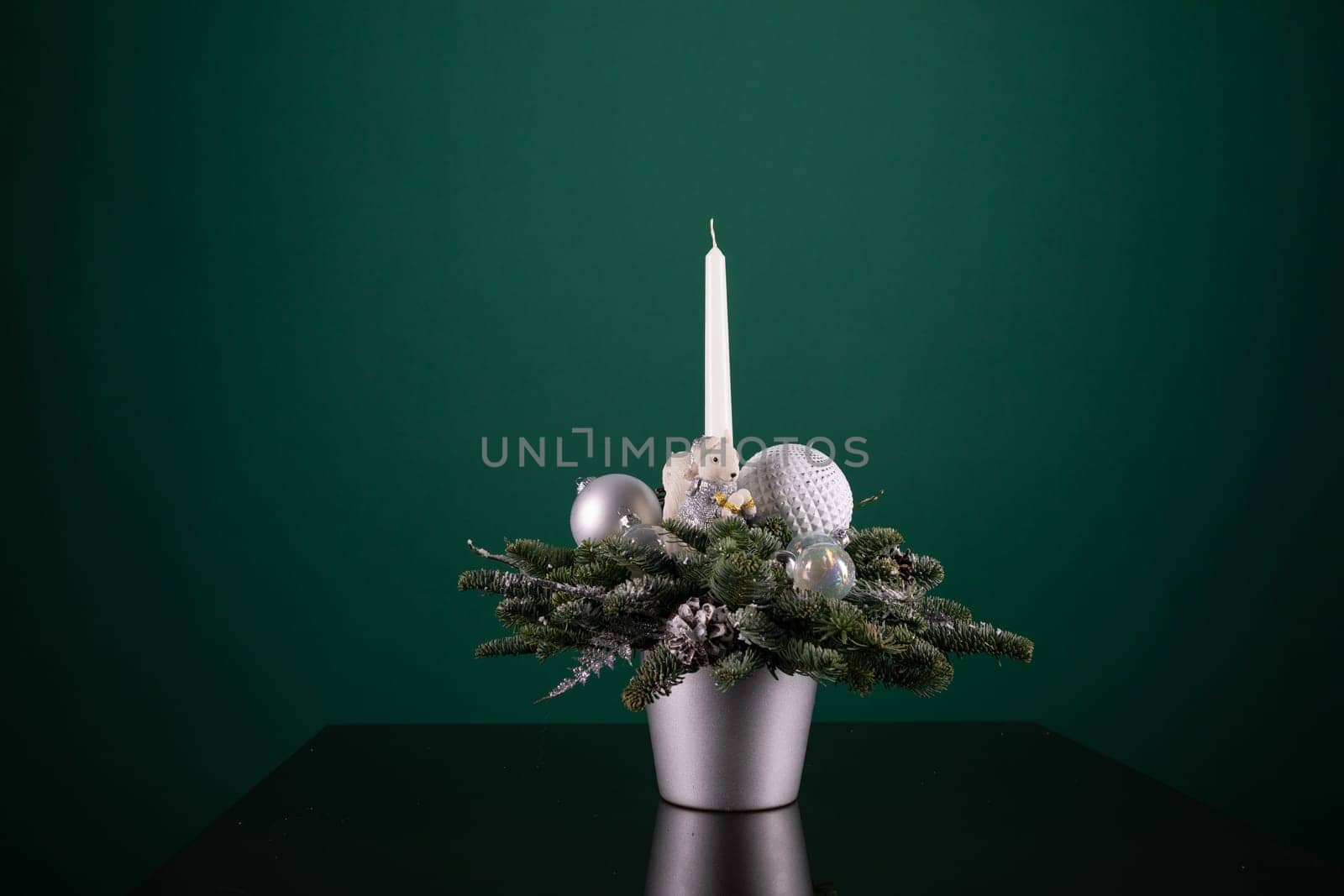 A silver vase containing a variety of Christmas decorations such as baubles, ribbons, and ornaments, alongside a white candle burning brightly. The scene is festive and adds a touch of holiday cheer to any room.