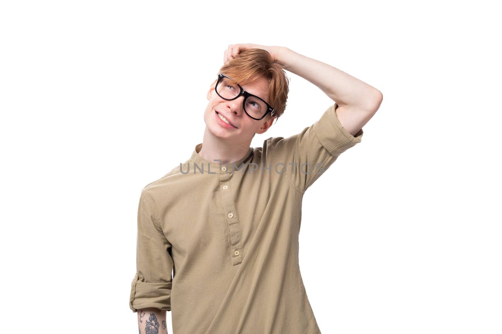 young positive red-haired european man dressed in a light brown shirt with a tattoo on his arm.