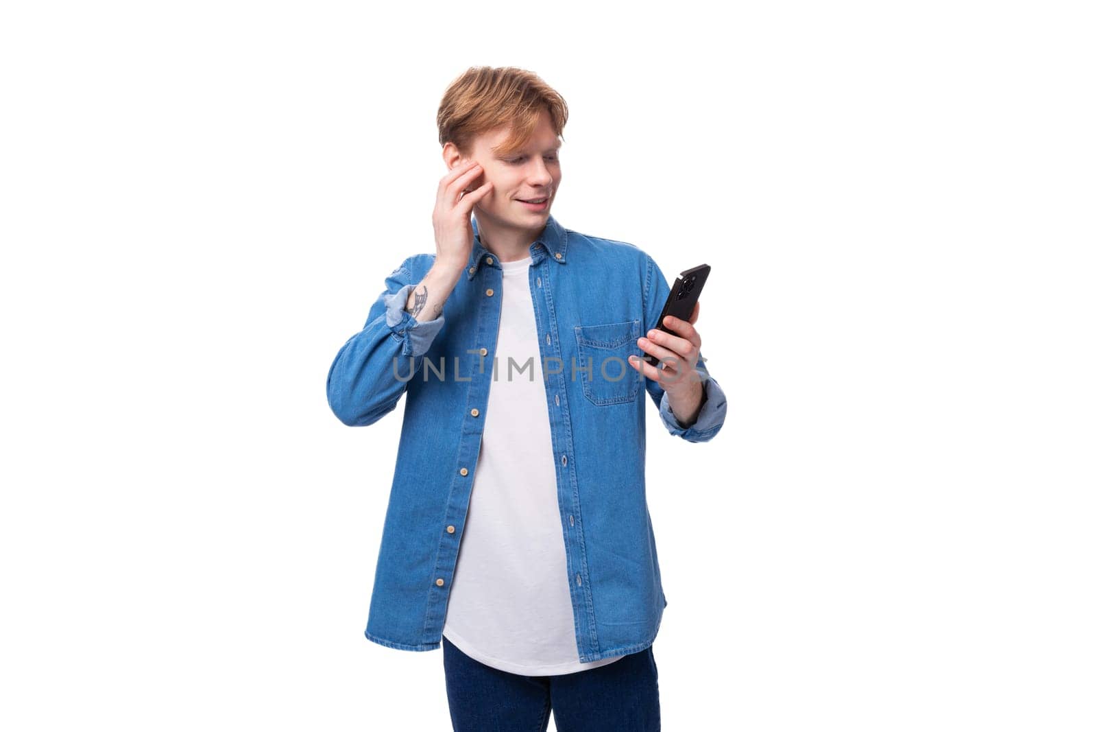 young redhead guy in a blue denim shirt writes a message on a smartphone.