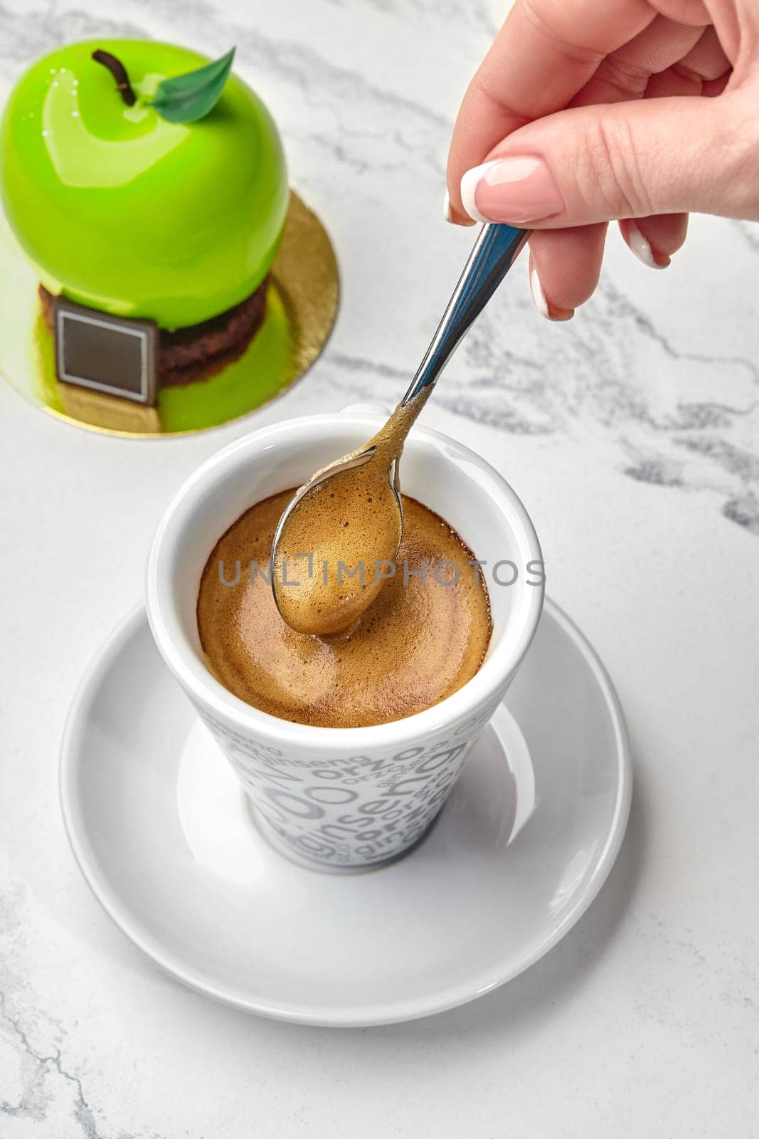 Female hand stirring espresso served with green apple-shaped pastry by nazarovsergey