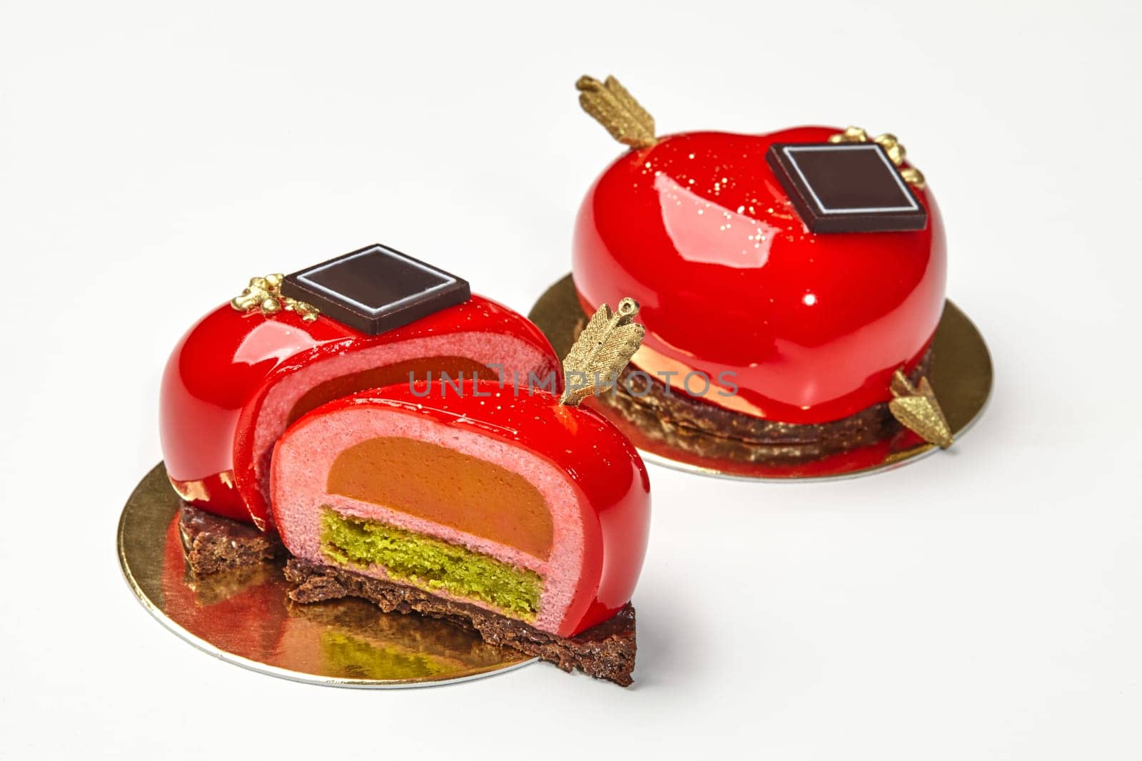 Closeup of sliced artisan dessert in shape of heart with golden arrow and layers of delicate berry mousse, sea buckthorn jelly and pistachio sponge on crispy chocolate streusel