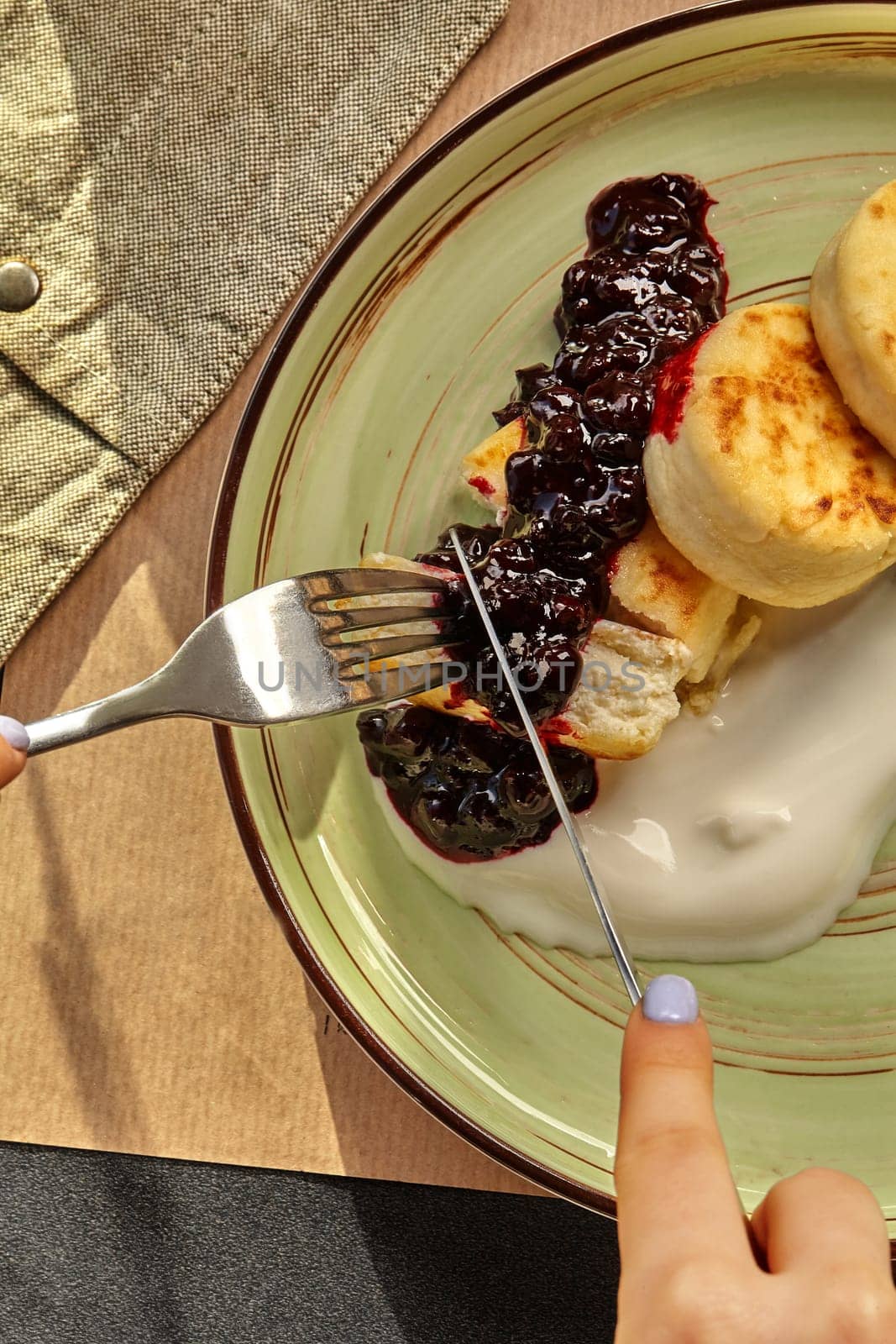 Female hands cutting into quark pancakes with berry sauce and sour cream by nazarovsergey