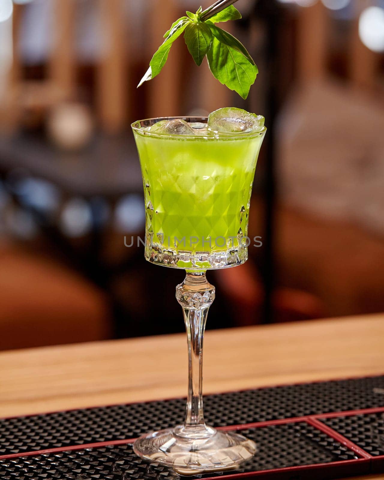 Elegantly presented glass of gin based Basil Smash cocktail with vibrant green color and fresh basil leaf garnish, served chilled on bar mat