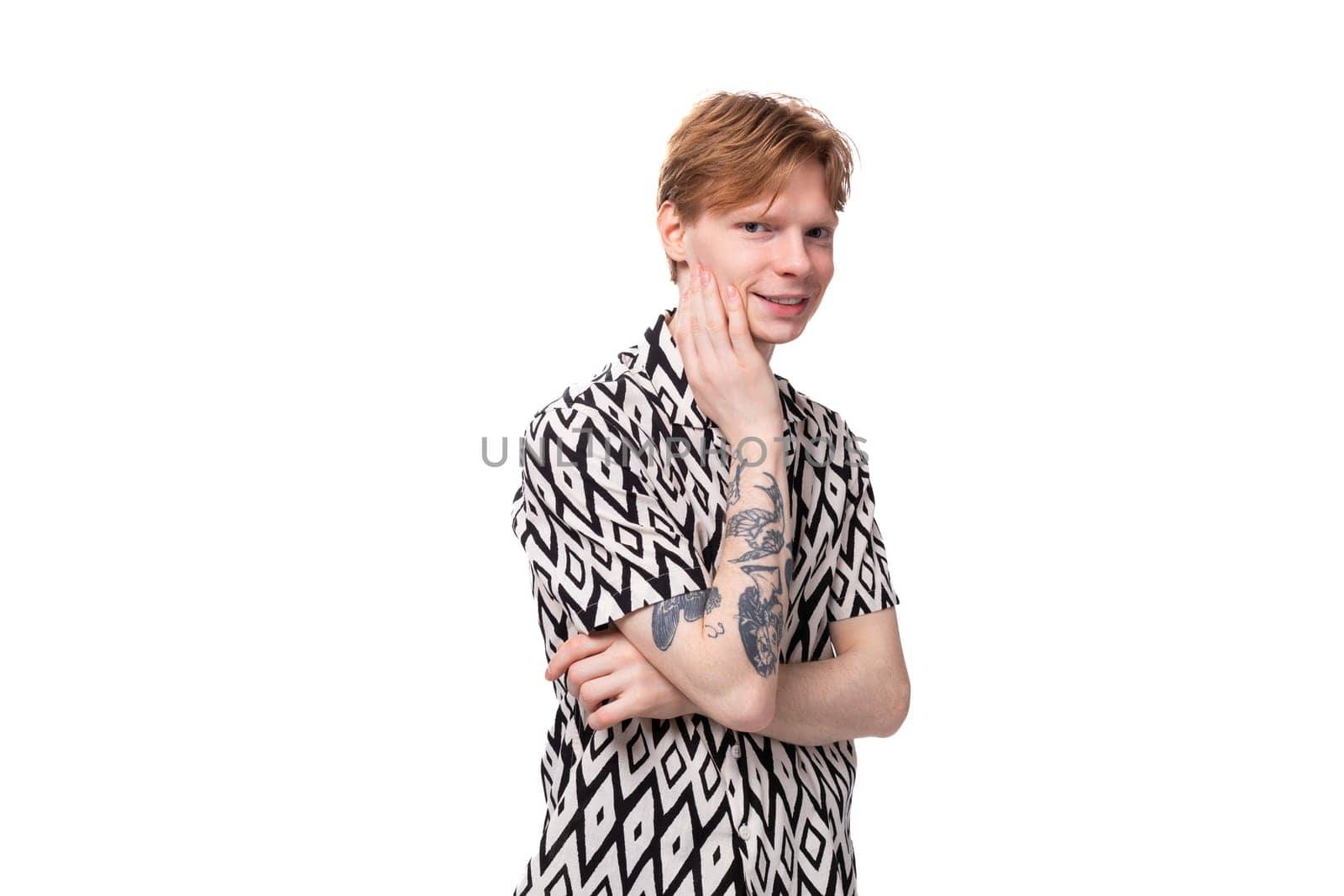 young positive caucasian man with red hair and a tattoo is dressed in a shirt with a rhombus pattern on a white background. people lifestyle concept.